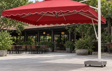 Dù tán vuông đỏ có diềm, trụ trắng bên phải và đế thấp trước khu bàn ghế được dọn xa