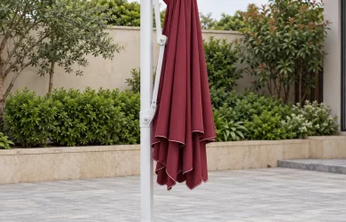 Tán dù đỏ xếp thành nếp dọc bên trụ trắng, bộ đỡ đã thu và đế vuông thấp trên sân khô