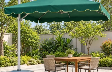 Minh họa dù lệch tâm vuông xanh viền vàng, khung bạc và đế có bánh xe che bàn bốn ghế ngoài sân