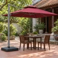 Dù lệch tâm tán vuông đỏ đô hai tầng, trụ xám bên trái và đế thấp cạnh bàn gỗ