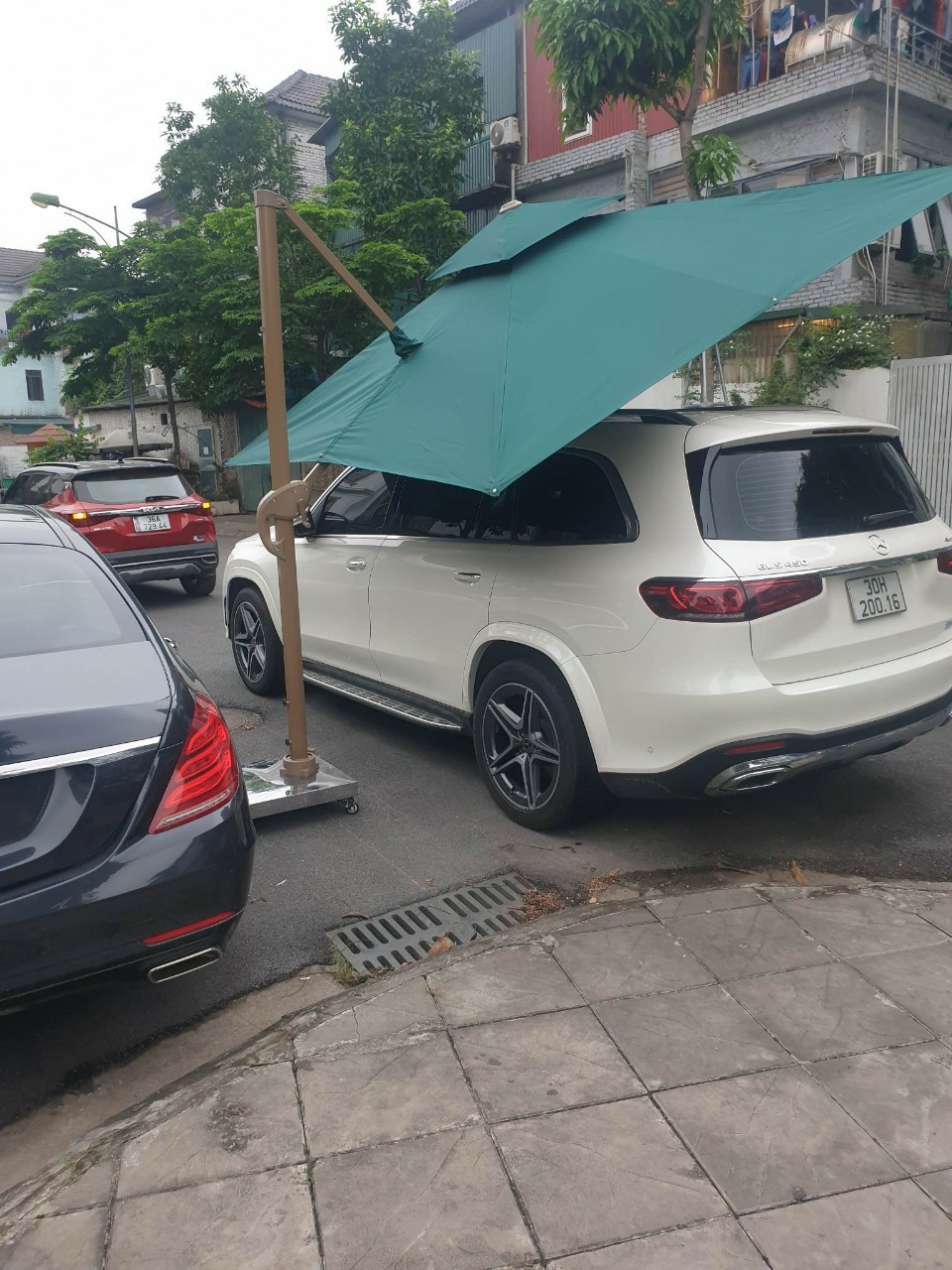 Ô lệch tâm tán xanh ở góc nghiêng bên cạnh một chiếc ô tô Ô lệch tâm tán xanh ở góc nghiêng bên cạnh một chiếc ô tô