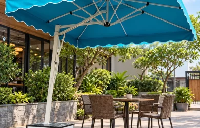 Minh họa ô lệch tâm tán vuông xanh có diềm, trụ bên và đế bánh xe cạnh bàn ngoài trời
